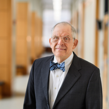 Portrait of Chazzan Steven Friedell standing in black jacket and white shirt with a blue bowtie.